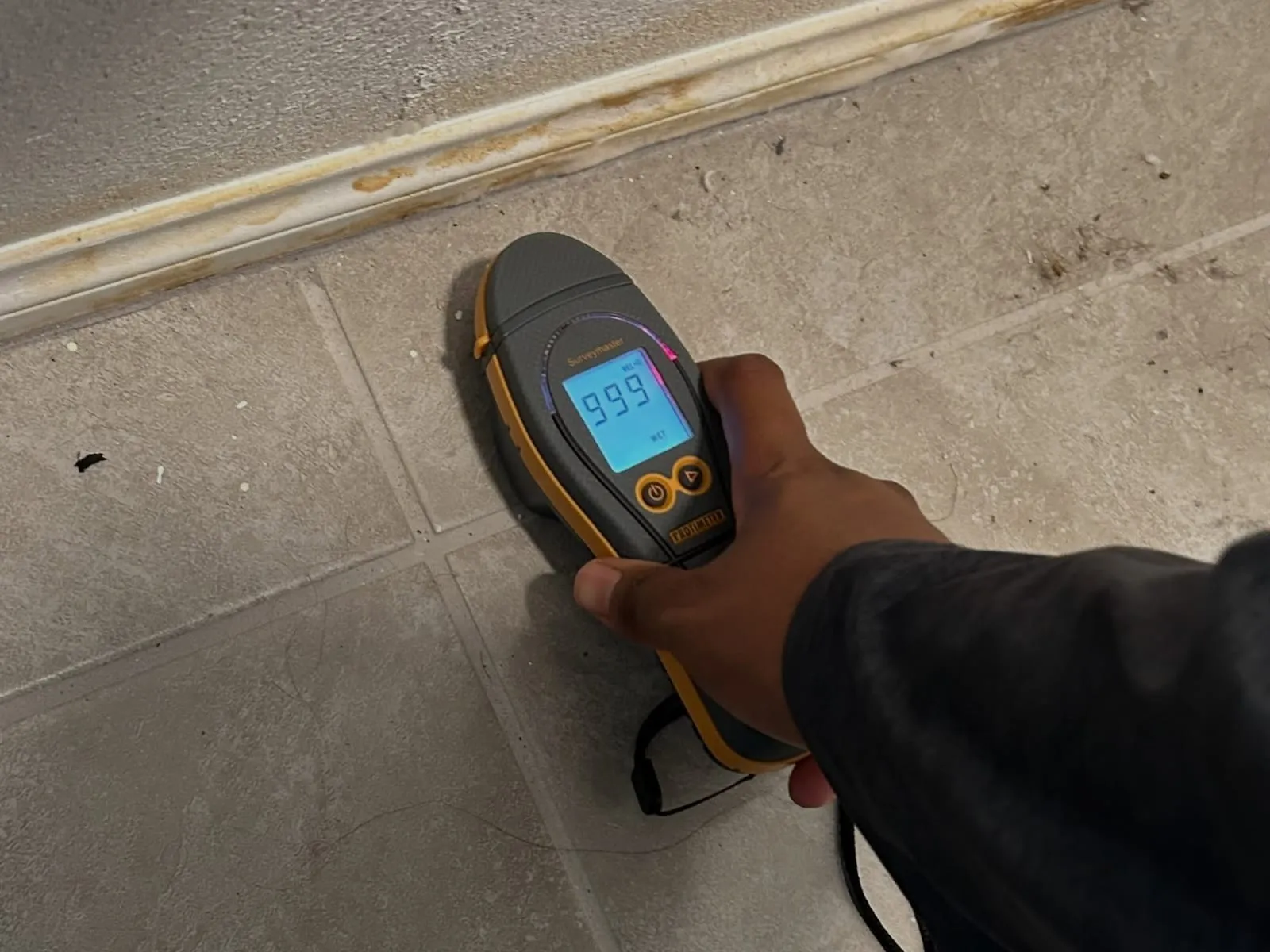 Hand holding a moisture meter against a basement wall